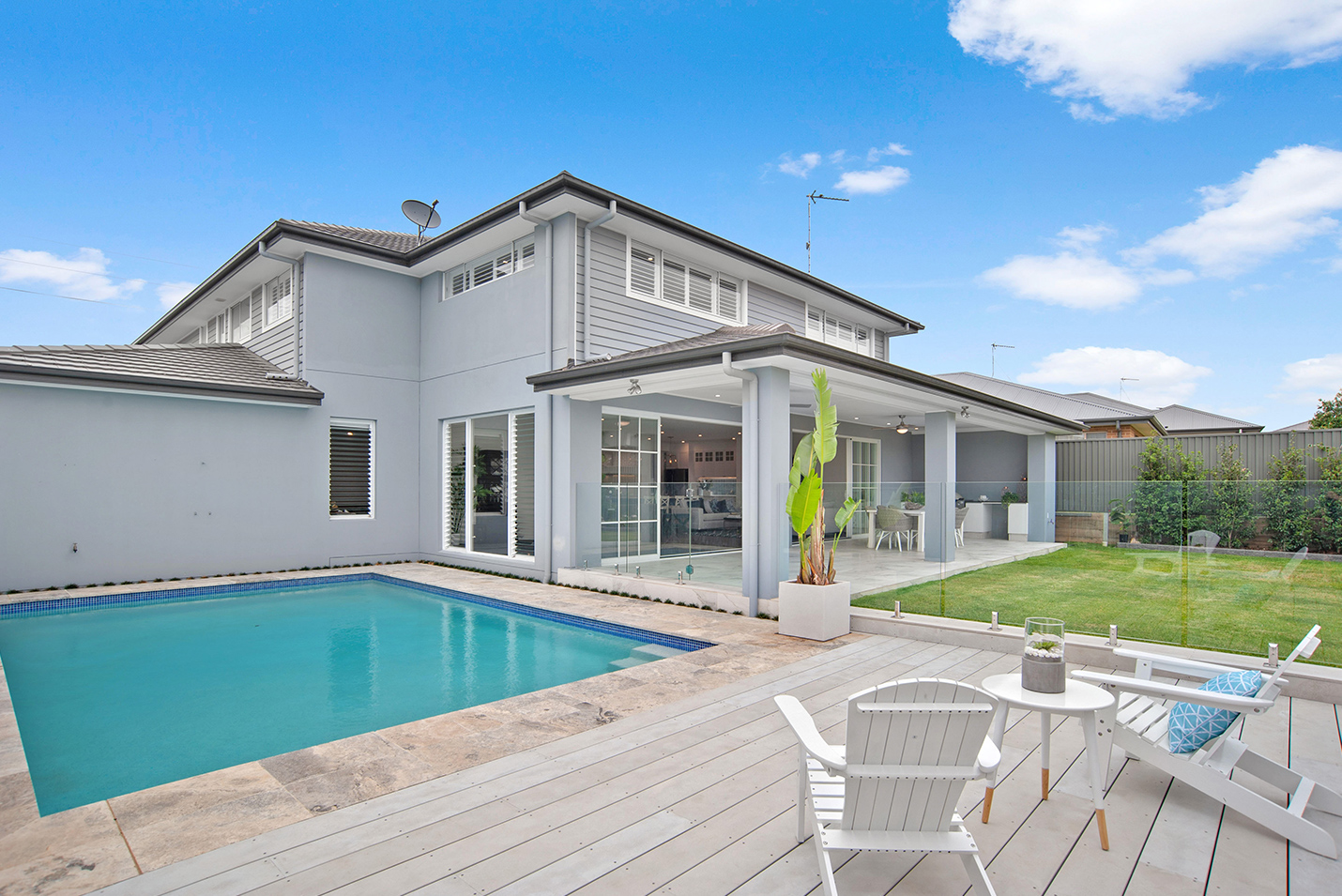 Pool deck view of Rosewood Hamptons Style home, with two deck chairs and a small table.